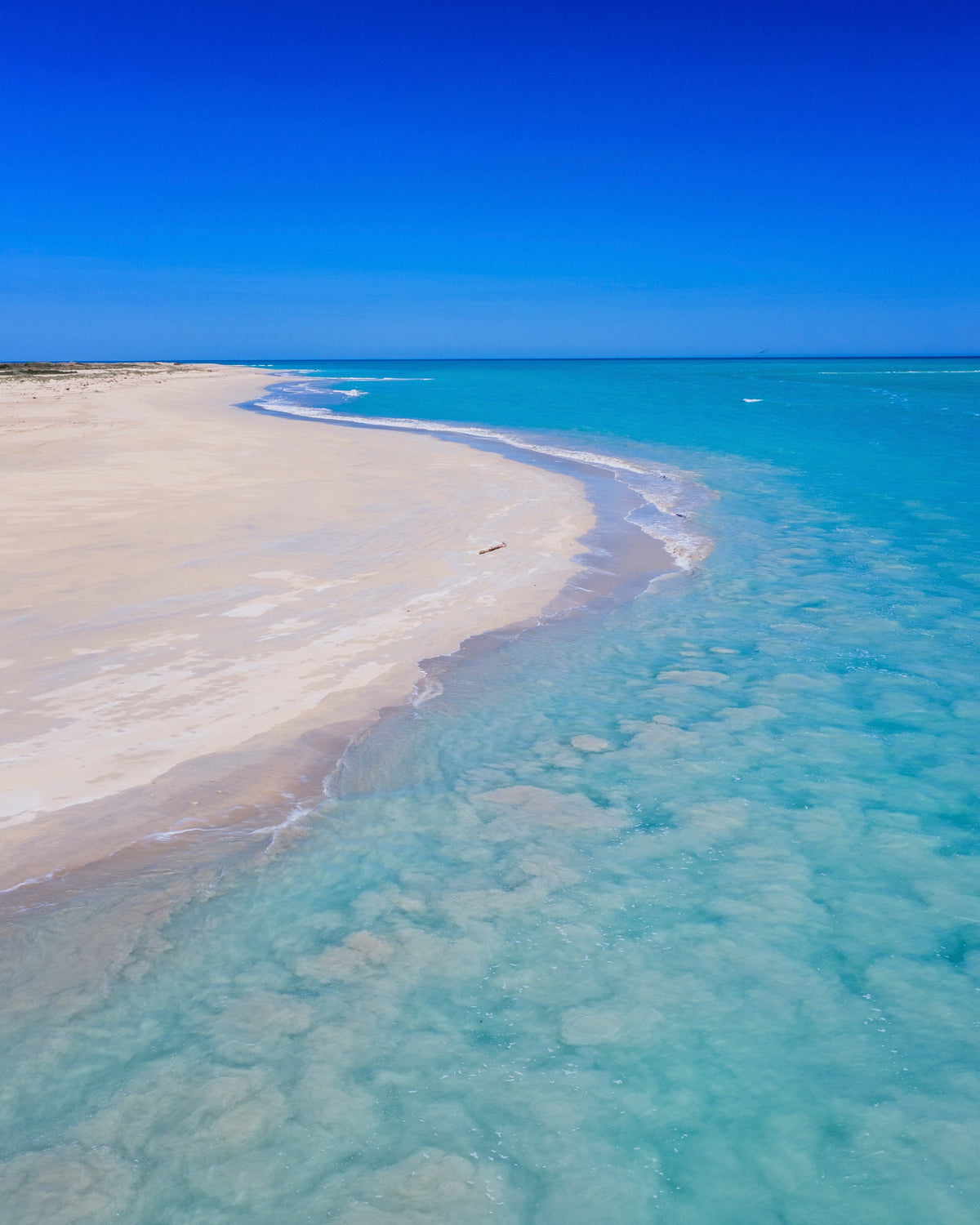 Aerial view of a sandy beach curving into turquoise ocean water under a clear blue sky.